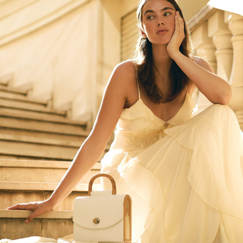Model in a light dress on stone steps with the BLACKWOOD Aurora White Saffiano handbag
